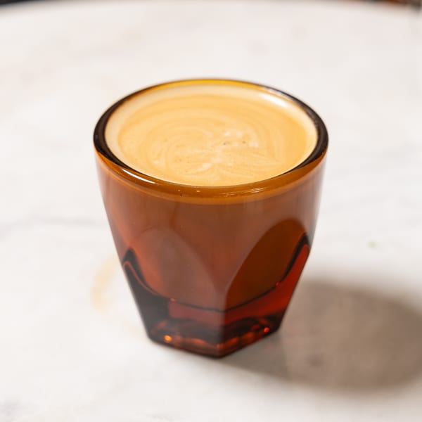 A rich espresso shot with creamy crema in a faceted amber glass on a white surface.