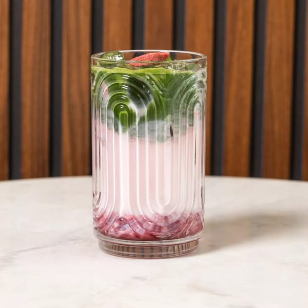 Layered pink and green drink in a textured glass with a red garnish on a marble table.