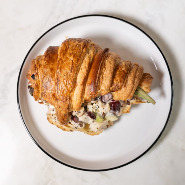 Golden croissant filled with chicken salad, grapes, and celery, on a white plate.
