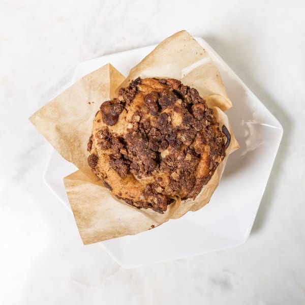 Overhead view of a chocolate chip muffin in a brown paper liner on a white plate.