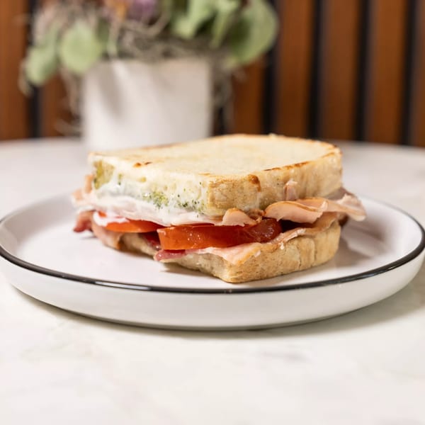 A grilled sandwich with bacon, tomato, and a creamy spread on a white plate.