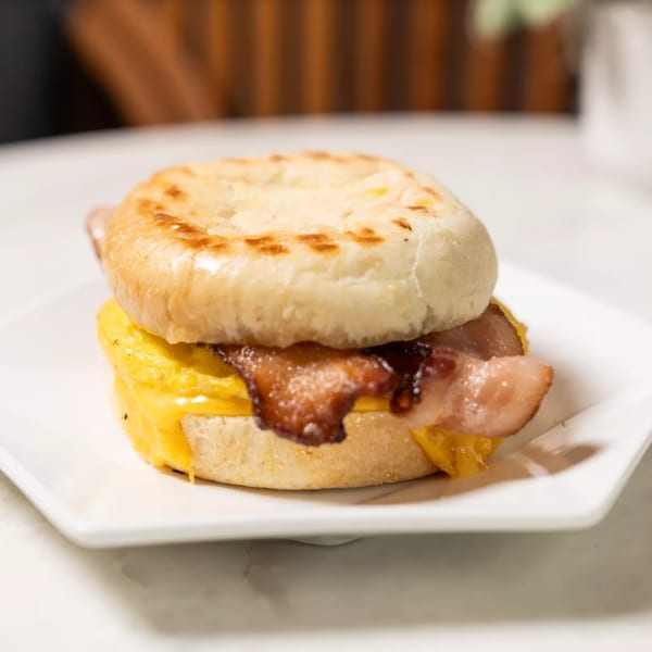 Breakfast sandwich with bacon, egg, and cheese on an English muffin, served on a white plate.