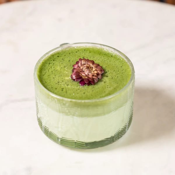 Green matcha latte in a textured glass, garnished with a dried flower on a white marble surface.
